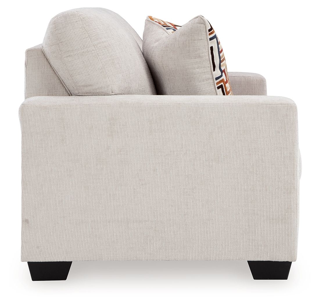 Light beige loveseat with two stacked back cushions and patterned throw pillow.
