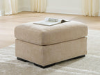 Beige fabric ottoman with rounded lid and black legs, with a magazine on top