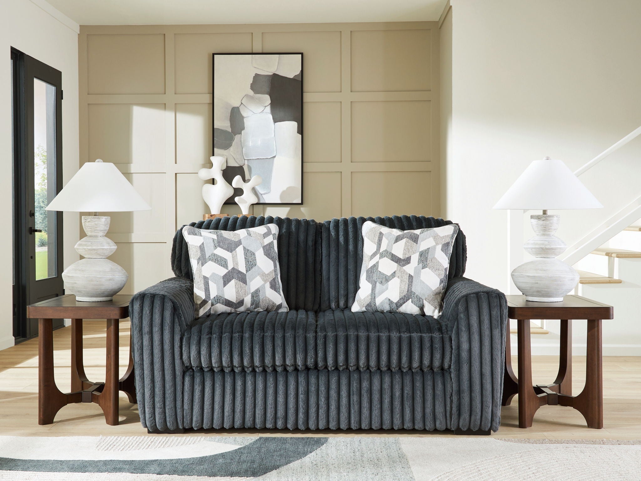 Dark gray corduroy loveseat with two patterned throw pillows in a living room