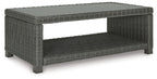 Gray rectangular cocktail table with woven frame and open-sided cushioned shelf