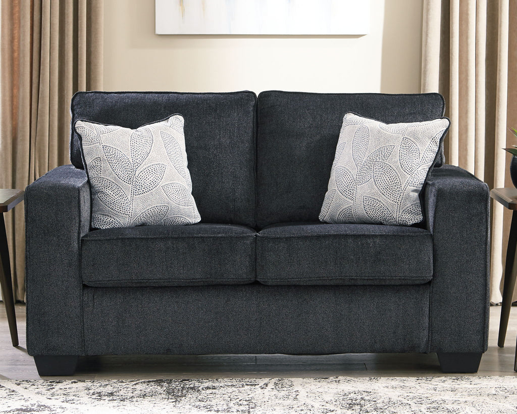 Dark gray loveseat with two white patterned throw pillows and padded square arms