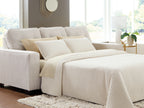 Queen sofa sleeper with light gray upholstery and beige bedding with two back pillows