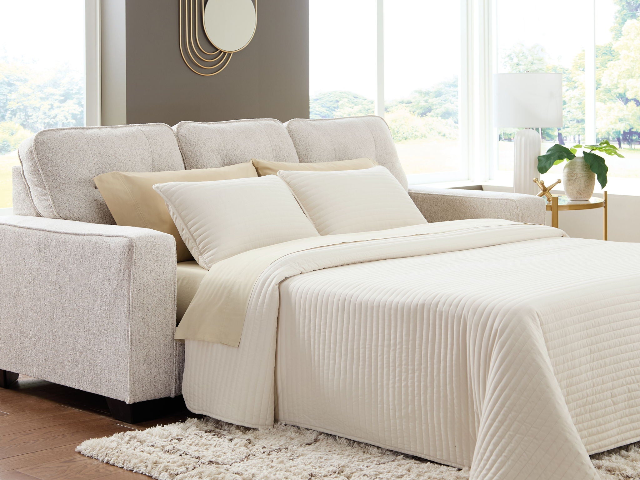 Queen sofa sleeper with light gray upholstery and beige bedding with two back pillows