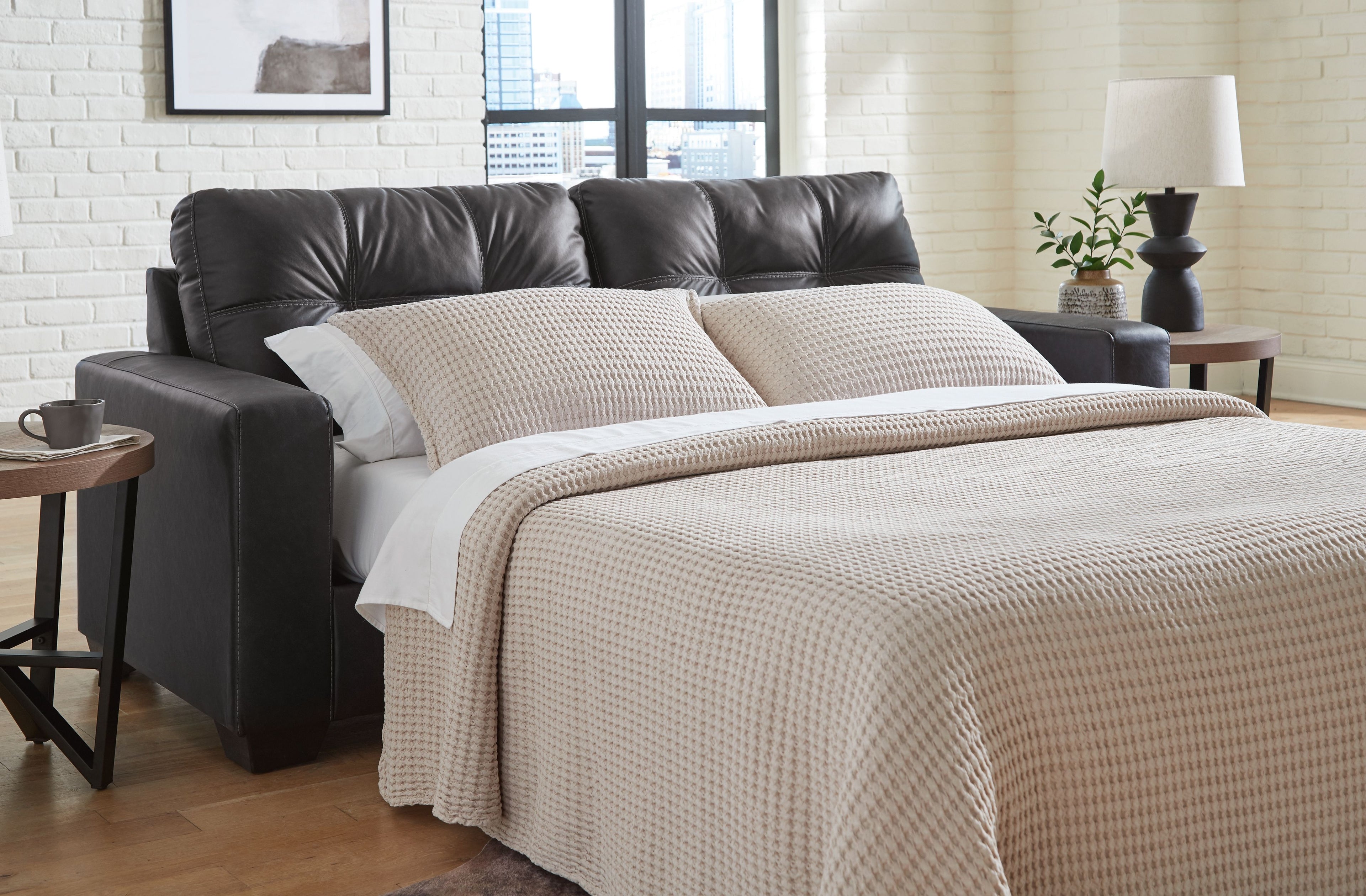 Dark brown sofa sleeper with tufted back and seat cushions, track arms; shown with bedding.