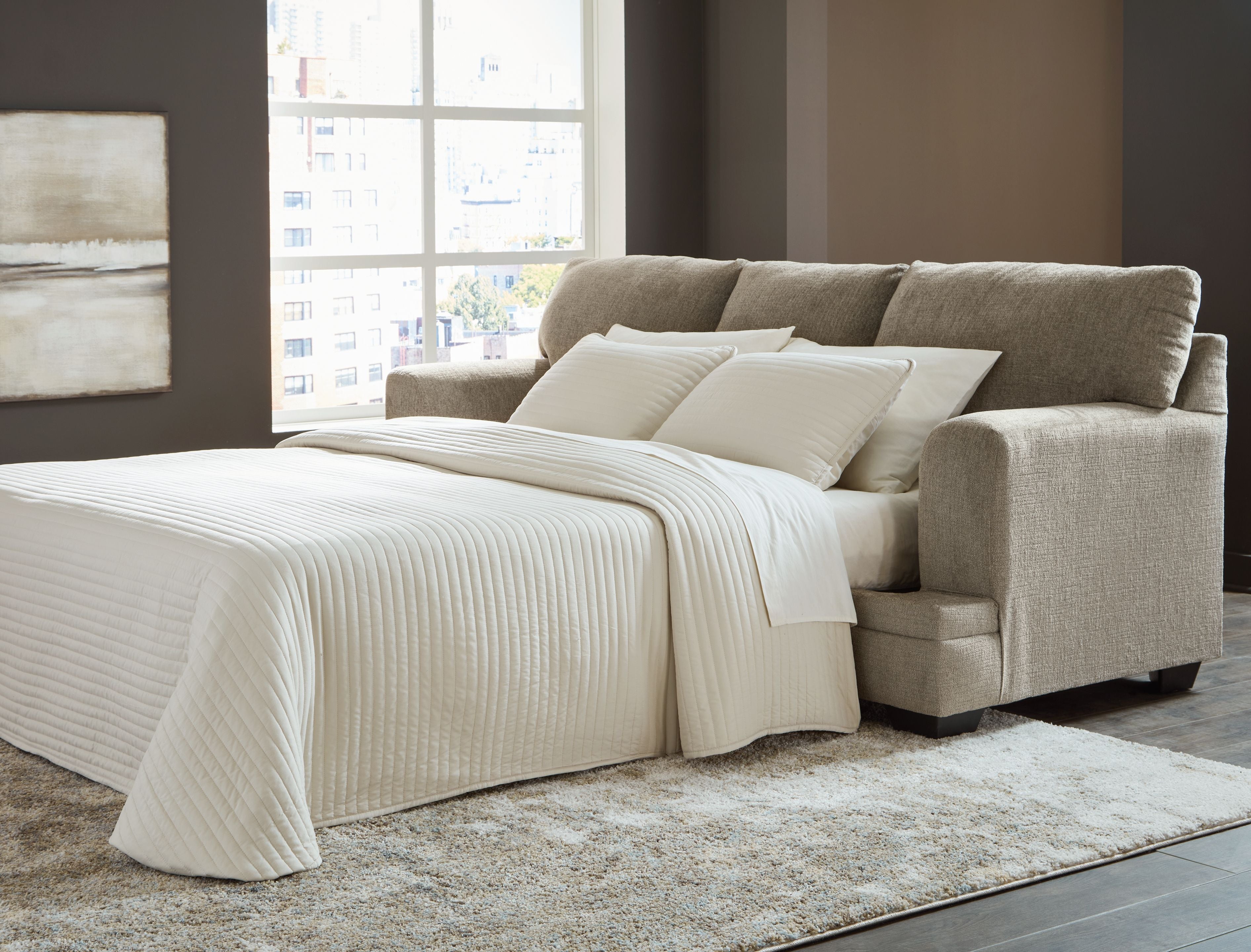 Sofa sleeper opened into a bed with cream bedding and two matching pillows on taupe upholstery