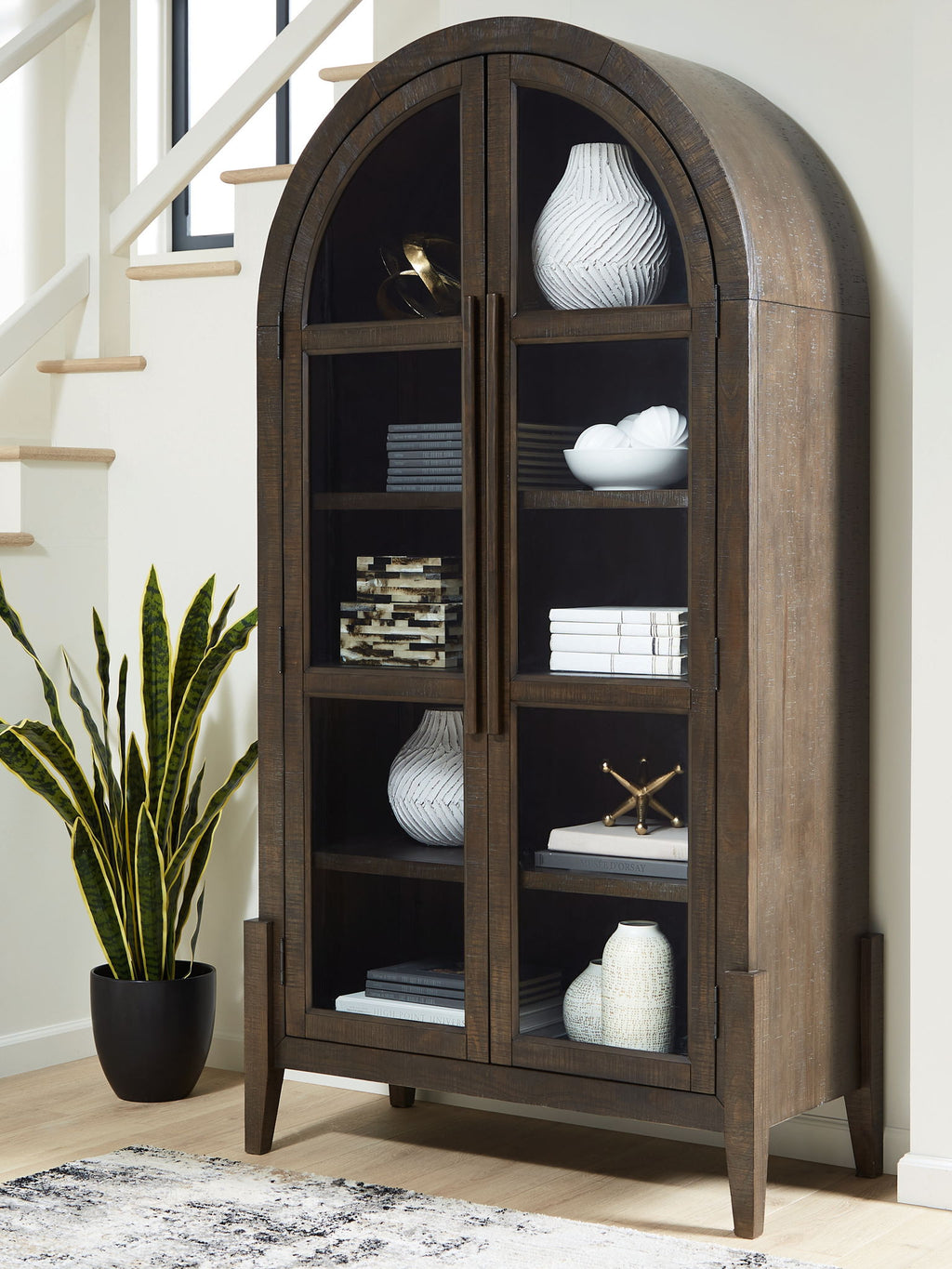 Dark brown accent cabinet with arched doors and open shelving with decor items inside