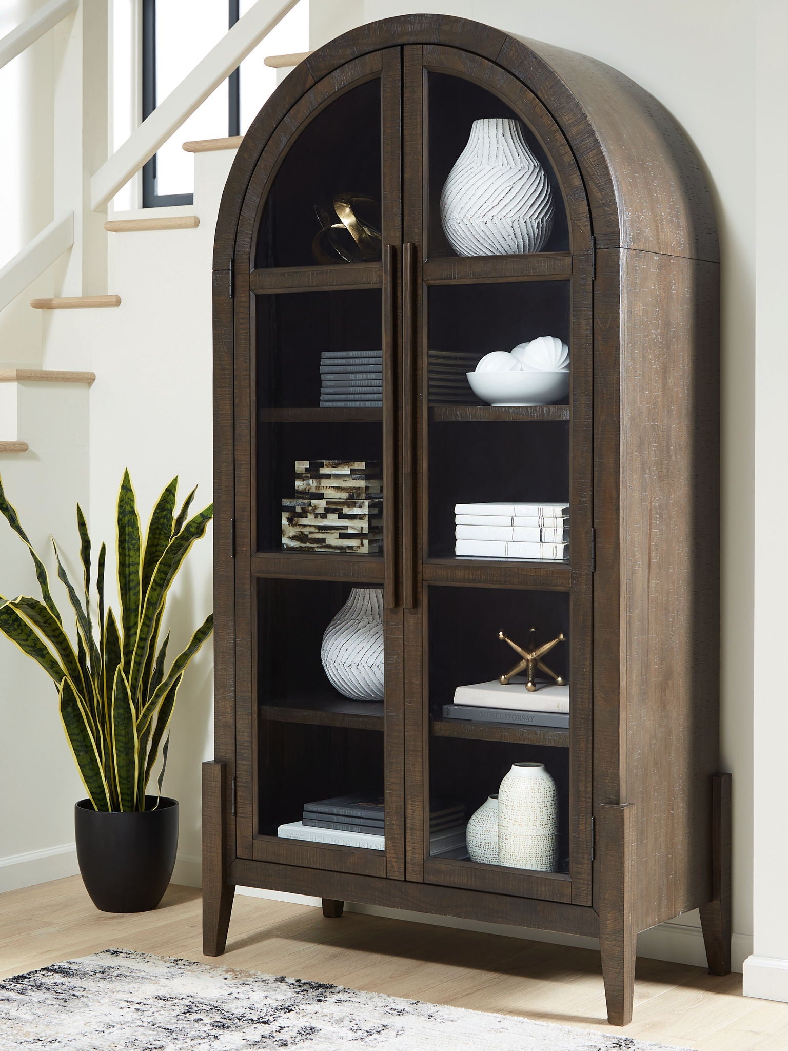 Dark brown accent cabinet with arched doors and open shelving with decor items inside