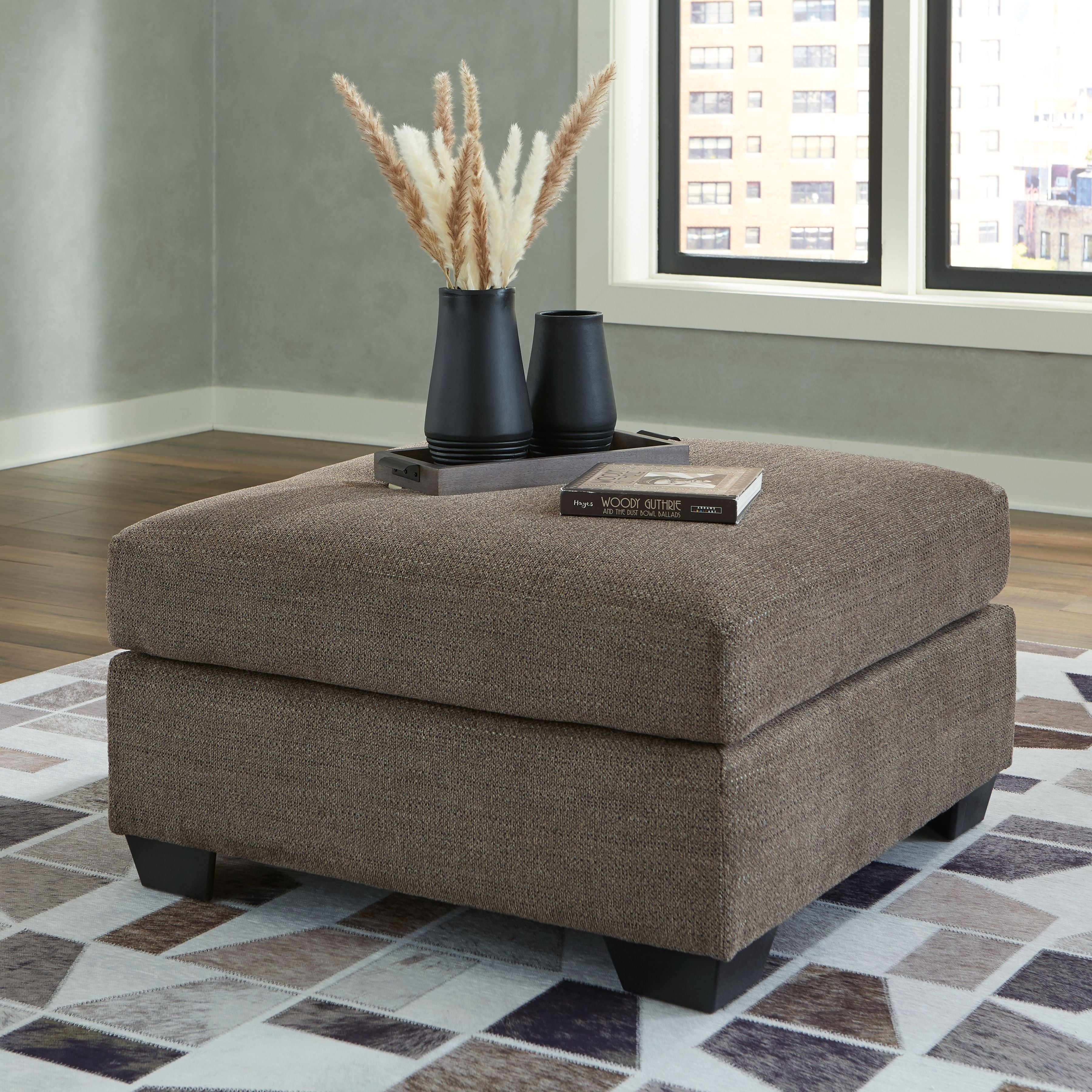 Oversized ottoman with light beige fabric, thick cushioned seat and squared black legs.