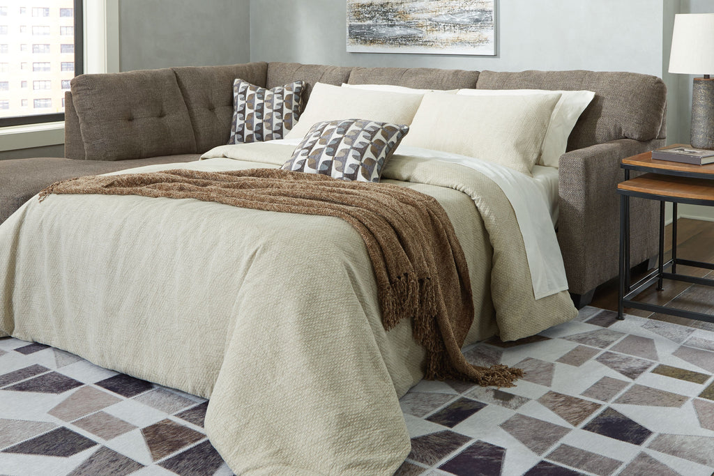 Sofa sleeper opened to a bed with dark gray backrest and layered throw pillows