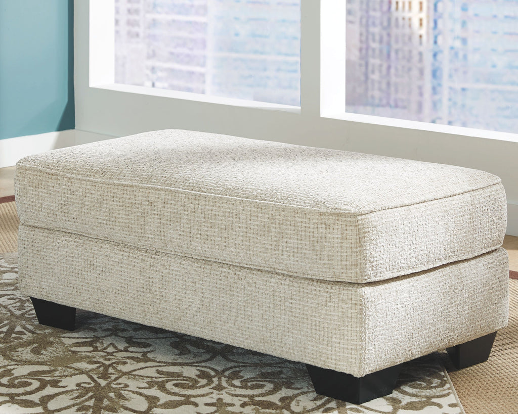 Sandstone upholstered ottoman with cushioned top seam and dark legs