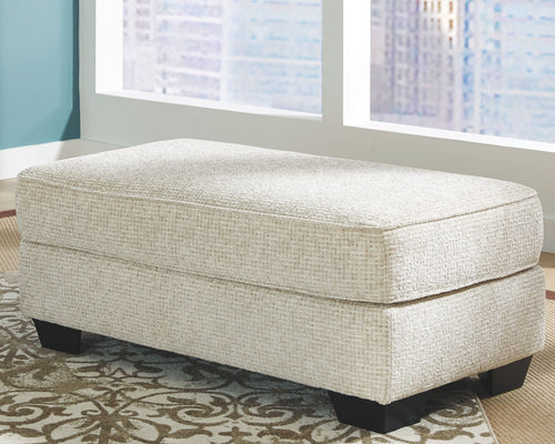 Sandstone upholstered ottoman with cushioned top seam and dark legs
