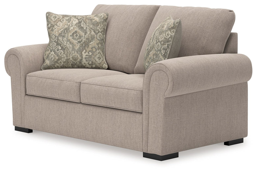 Beige loveseat with curved rolled arms, two seat cushions, and three patterned throw pillows