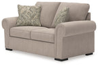 Beige loveseat with curved rolled arms, two seat cushions, and three patterned throw pillows