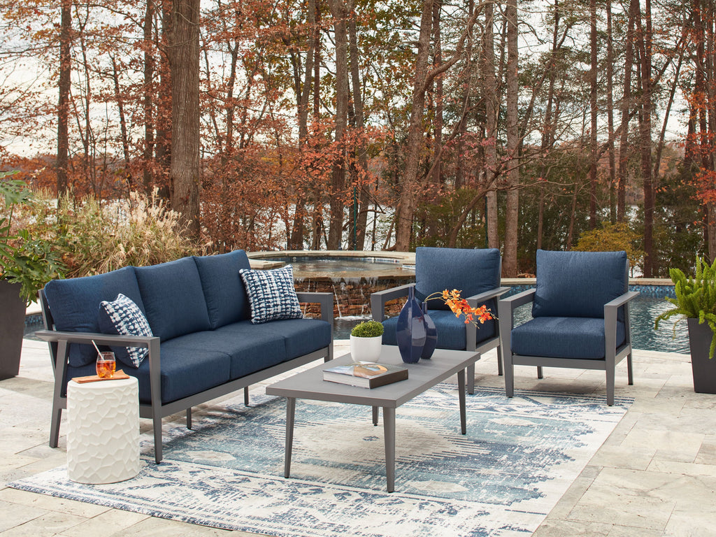 Outdoor seating set with navy loveseat, two armchairs, and gray-framed table with glass top