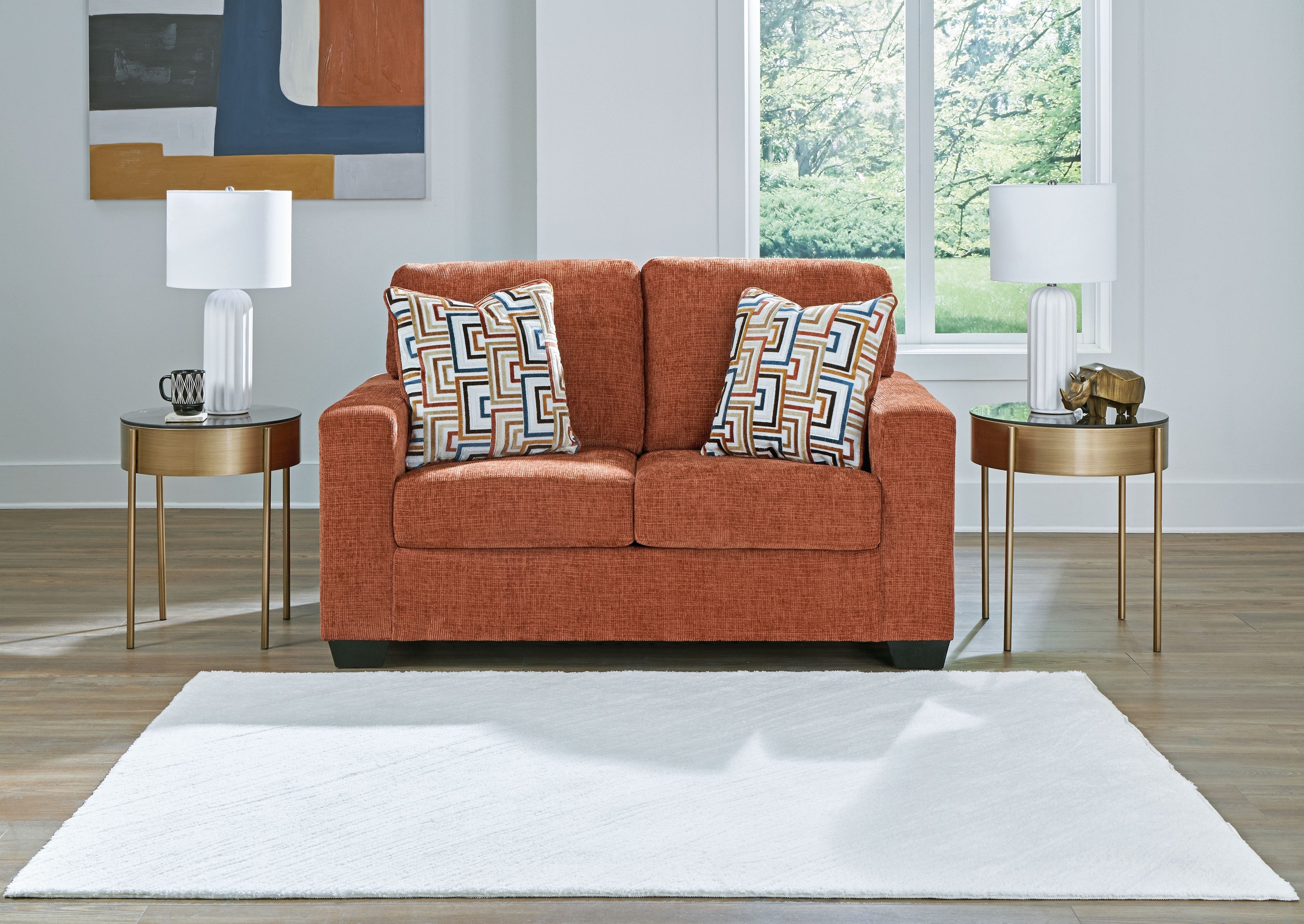 Rust orange loveseat with two decorative patterned throw pillows and straight seat.