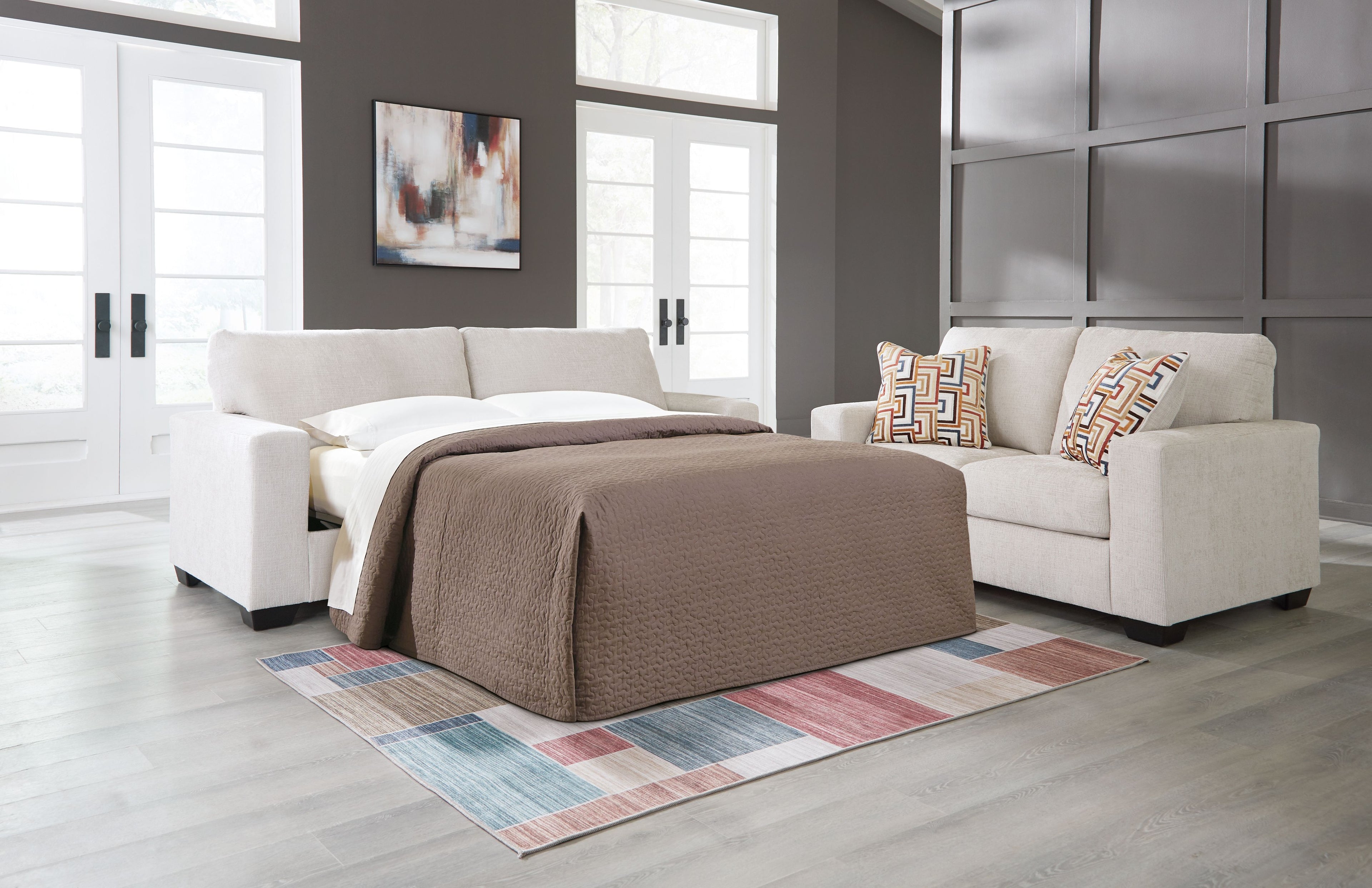 Stone sofa sleeper with bed base and two patterned pillows, made up with bedding.
