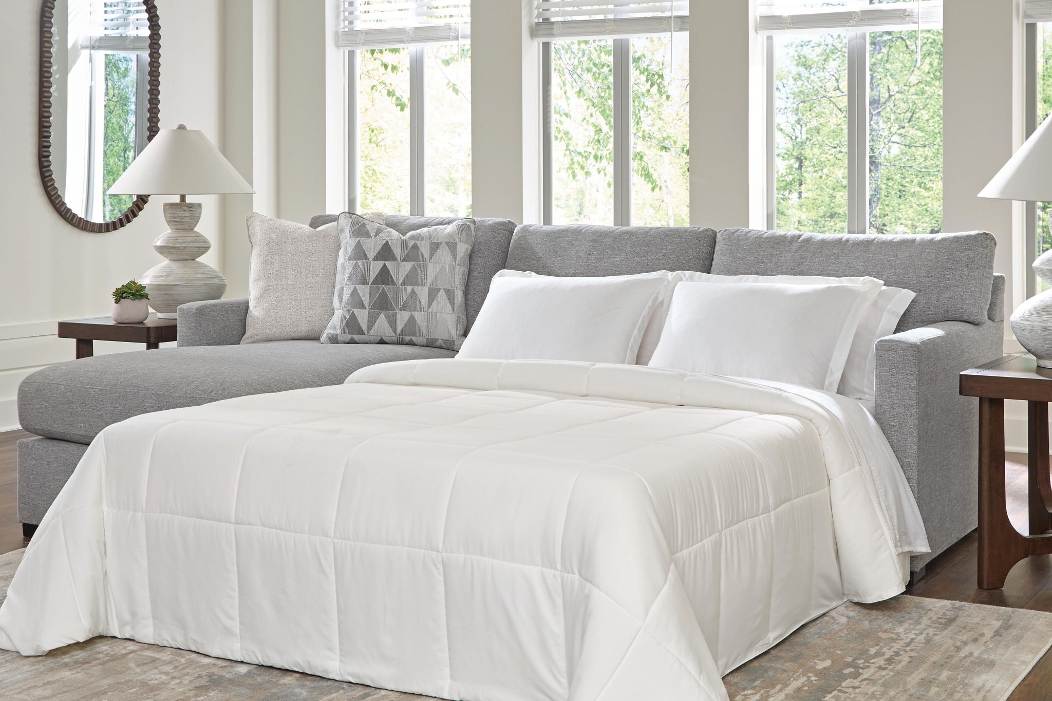 Dark gray sleeper sectional sofa with chaise, featuring an unfolded bed and white comforter