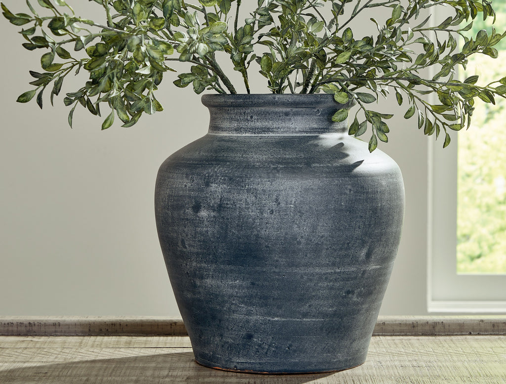Blue ceramic vase with wide opening holding green leaves branches