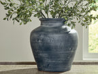 Blue ceramic vase with wide opening holding green leaves branches