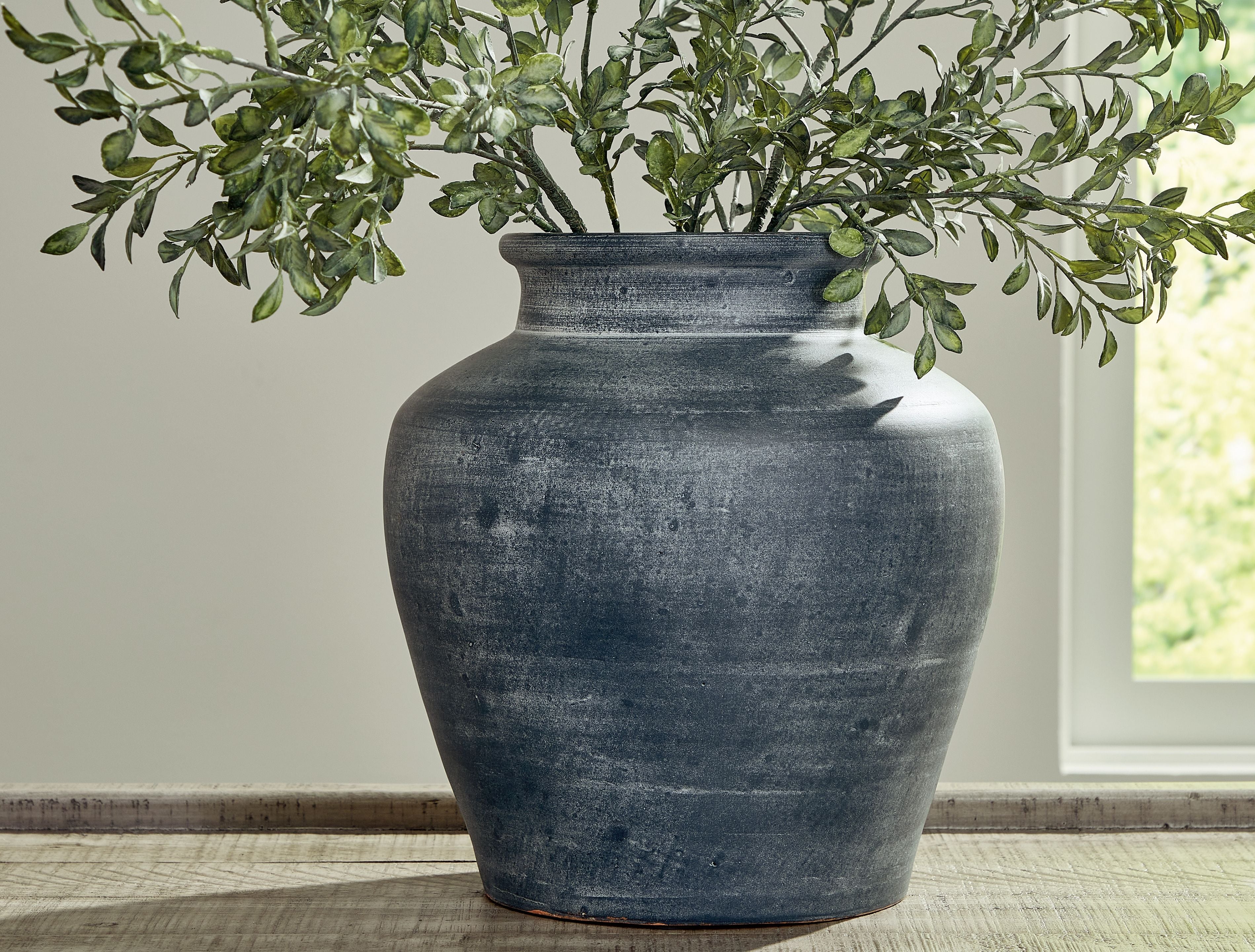 Blue ceramic vase with wide opening holding green leaves branches