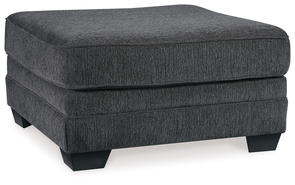 Slate gray upholstered ottoman with rounded top, padded sides, and dark legs