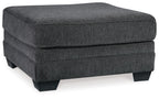 Slate gray upholstered ottoman with rounded top, padded sides, and dark legs