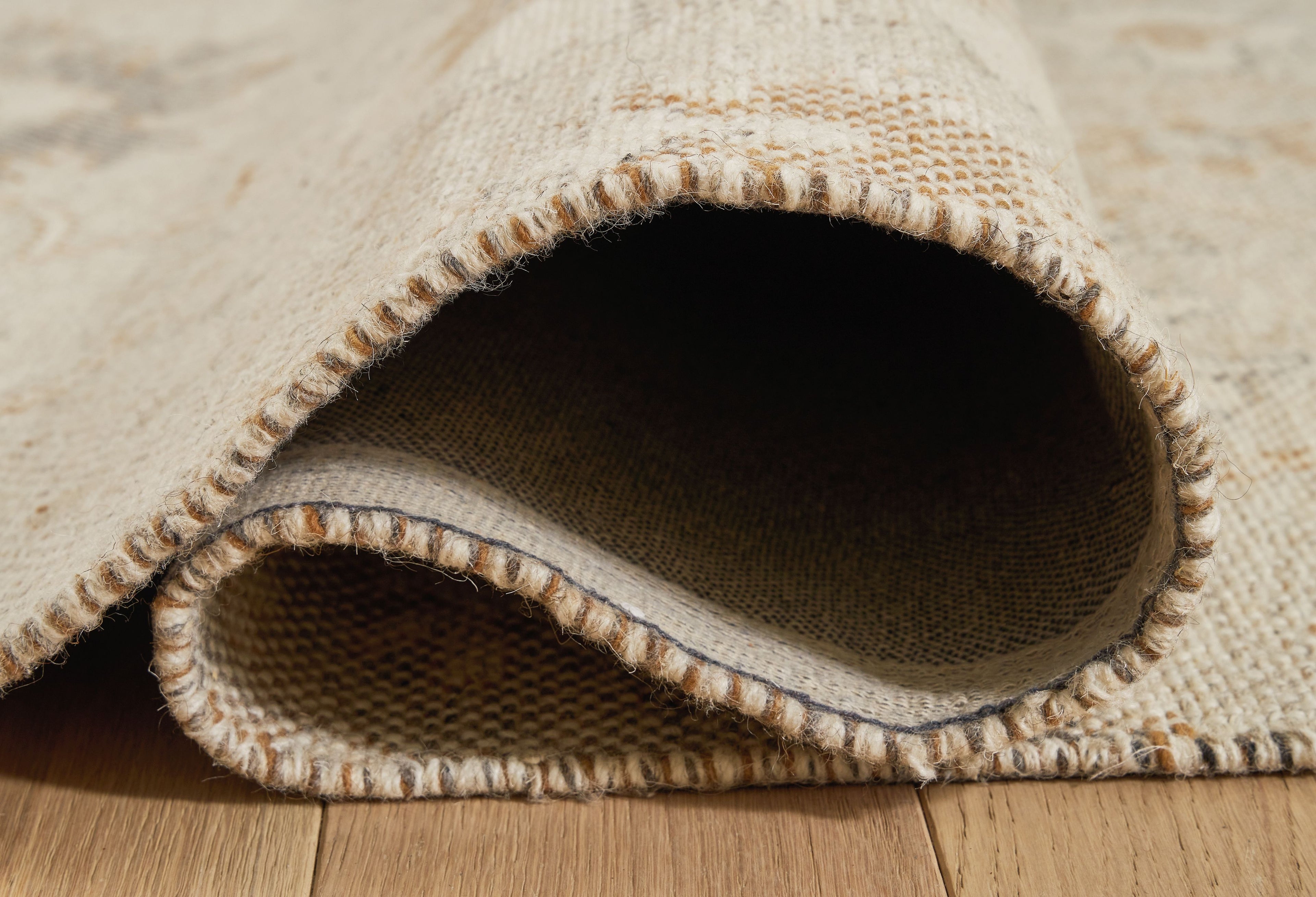 Beige rug edge with folded-over construction, showing underside and binding