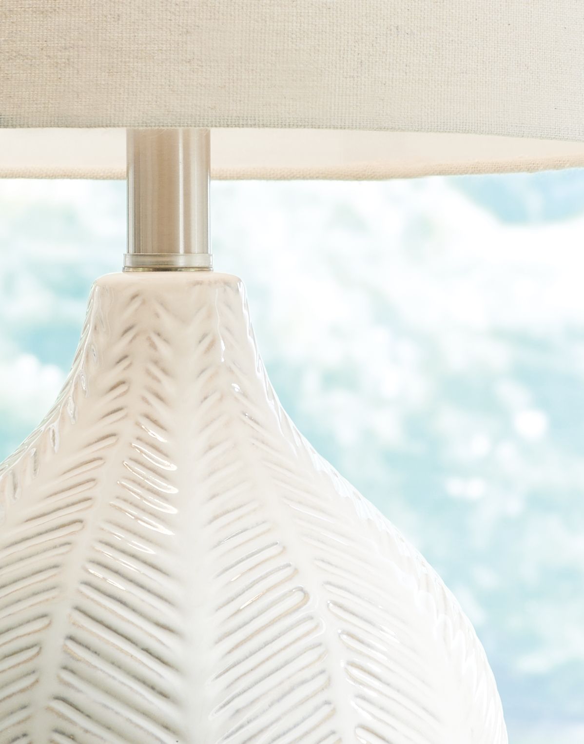 Ceramic table lamp base close-up with off-white textured pattern and metal stem