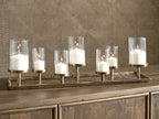 Antique brass candle holder with six lit candles and clear glass cylinders