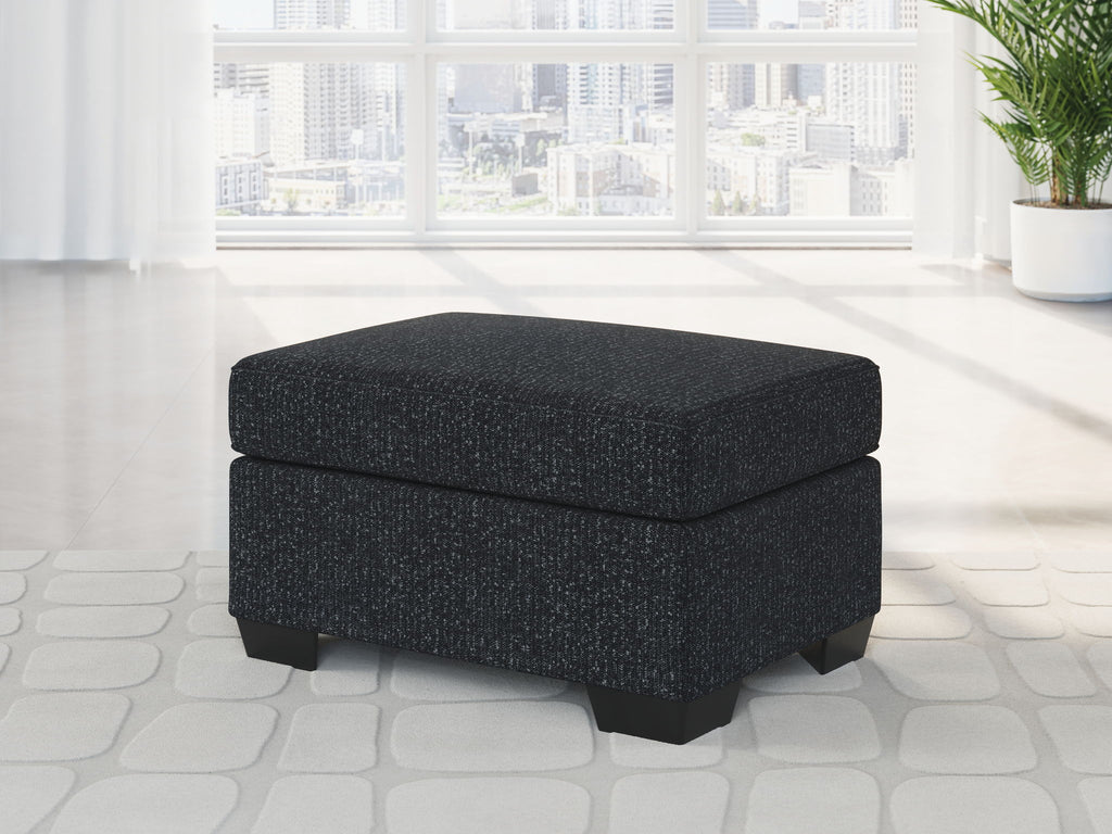 Square upholstered ottoman in dark fabric with cushioned lid and block legs