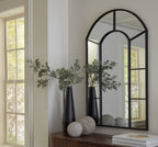 Black arched accent mirror with slim frame, standing against a wall