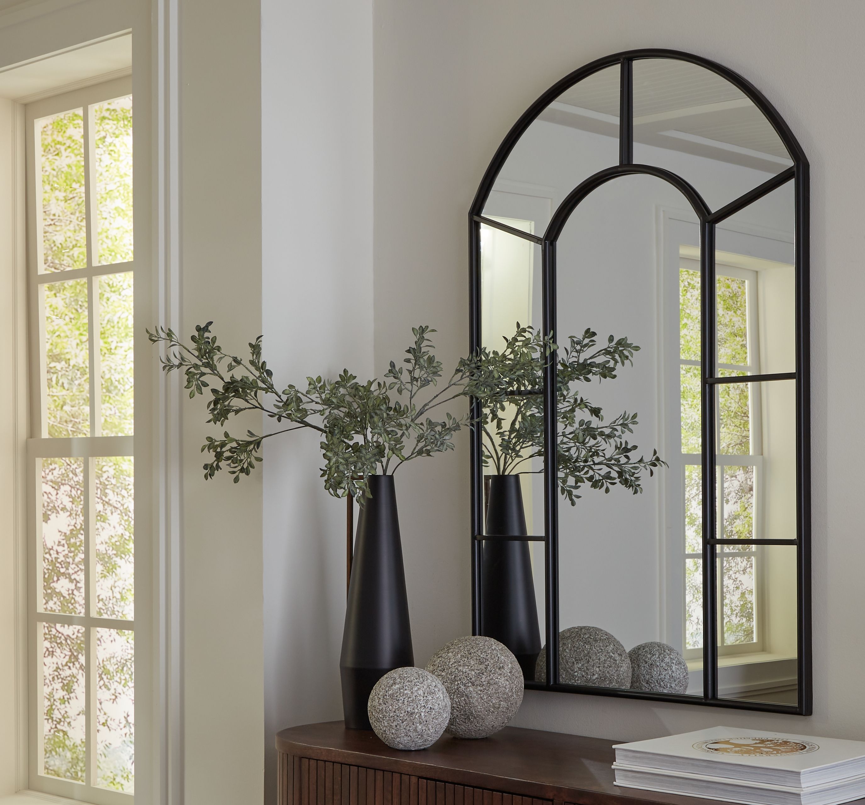 Black arched accent mirror with slim frame, standing against a wall