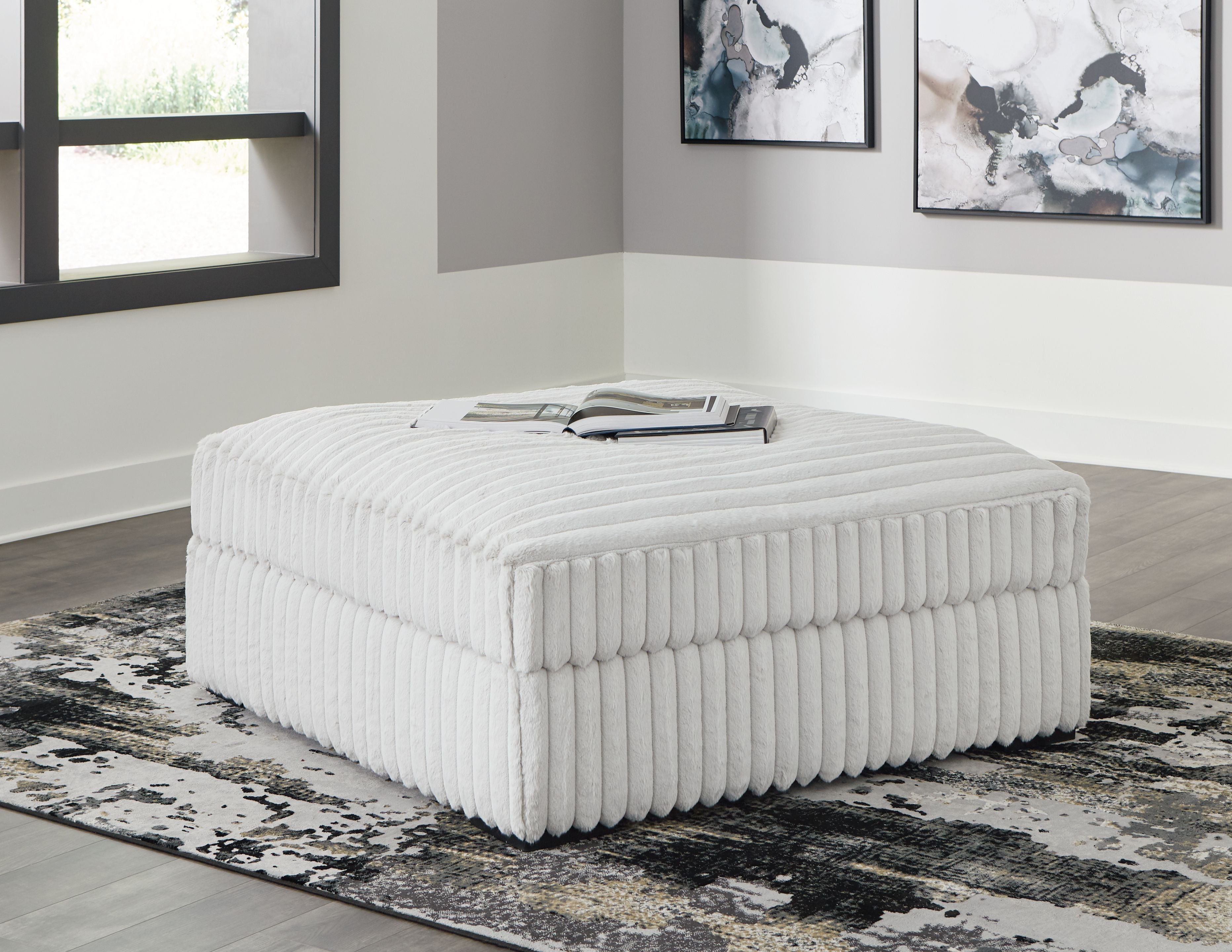 Oversized accent ottoman with light gray ribbed upholstery, square cushioned top