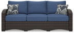 Outdoor sofa with blue seat cushions and back cushions, brown frame, two patterned pillows