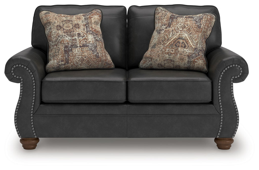 Dark gray loveseat with two patterned throw pillows and studded arm trim