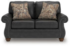 Dark gray loveseat with two patterned throw pillows and studded arm trim