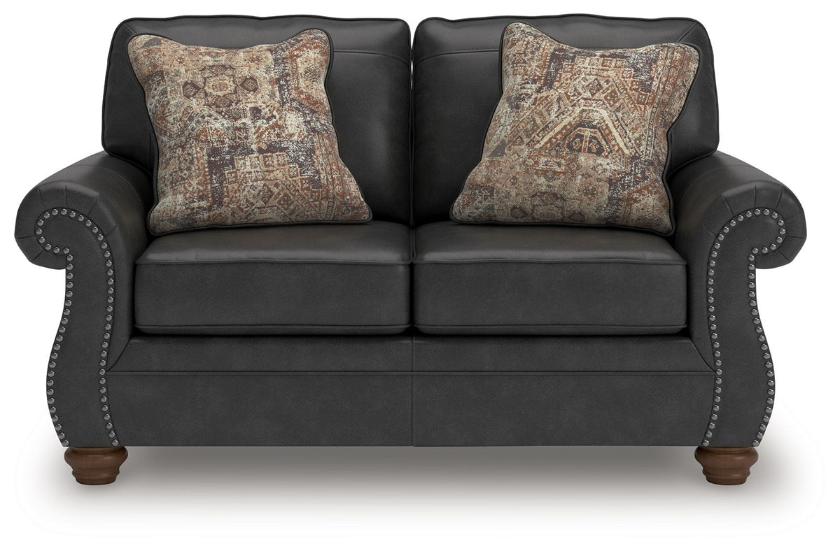 Dark gray loveseat with two patterned accent pillows and studded, curved armrests