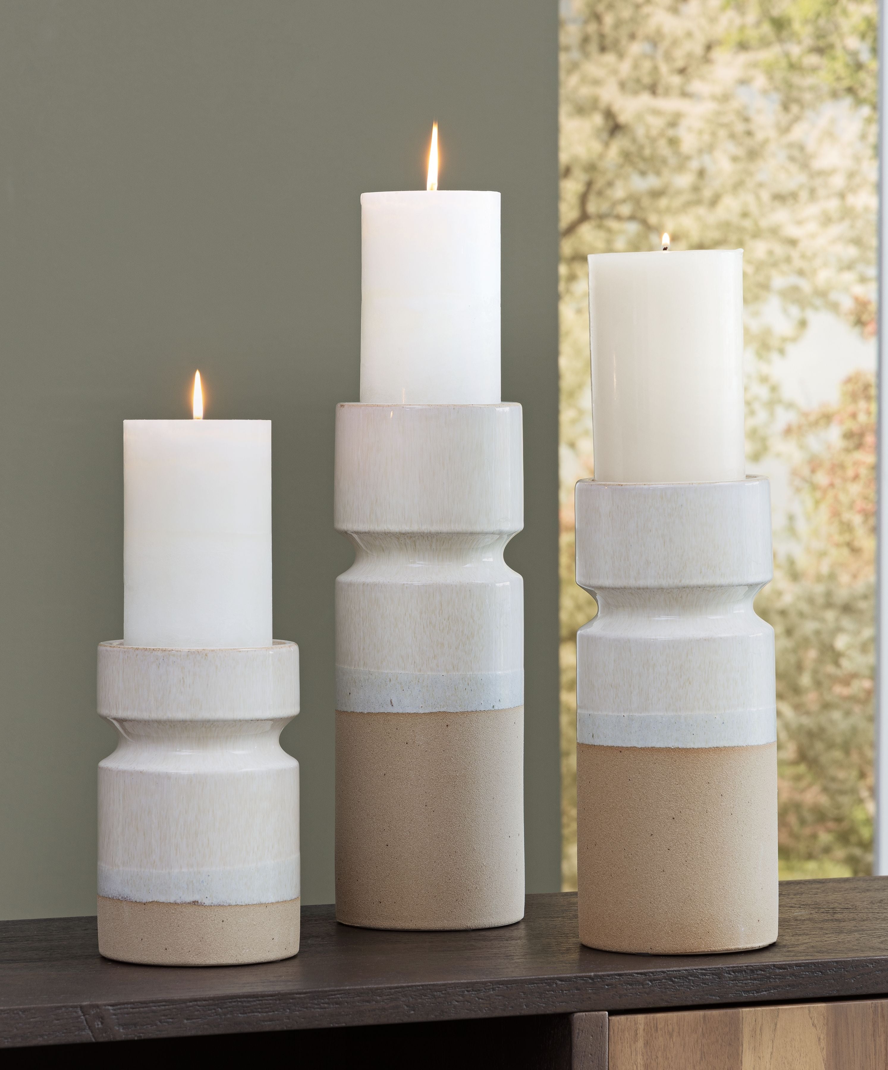 Set of 3 candle holders with lit white candles in ivory-and-brown stacked cylinders