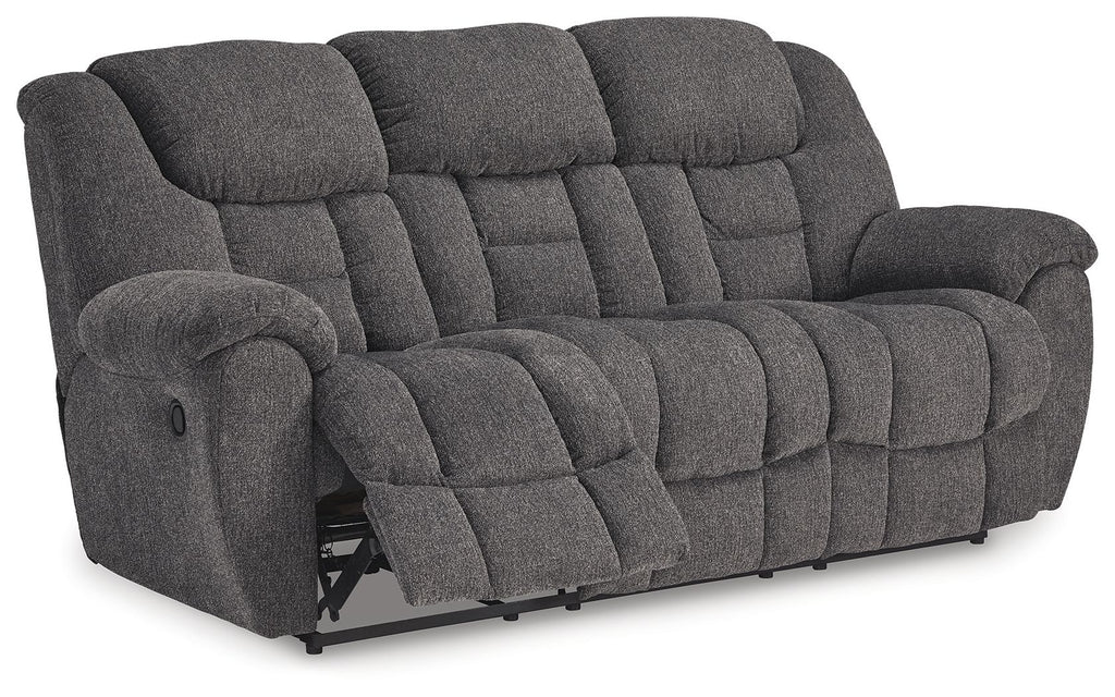 Dark gray reclining sofa with extended footrest, button-tufted cushions and arms