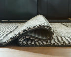 Black-and-white geometric rug with rolled edge, dense textured pile.