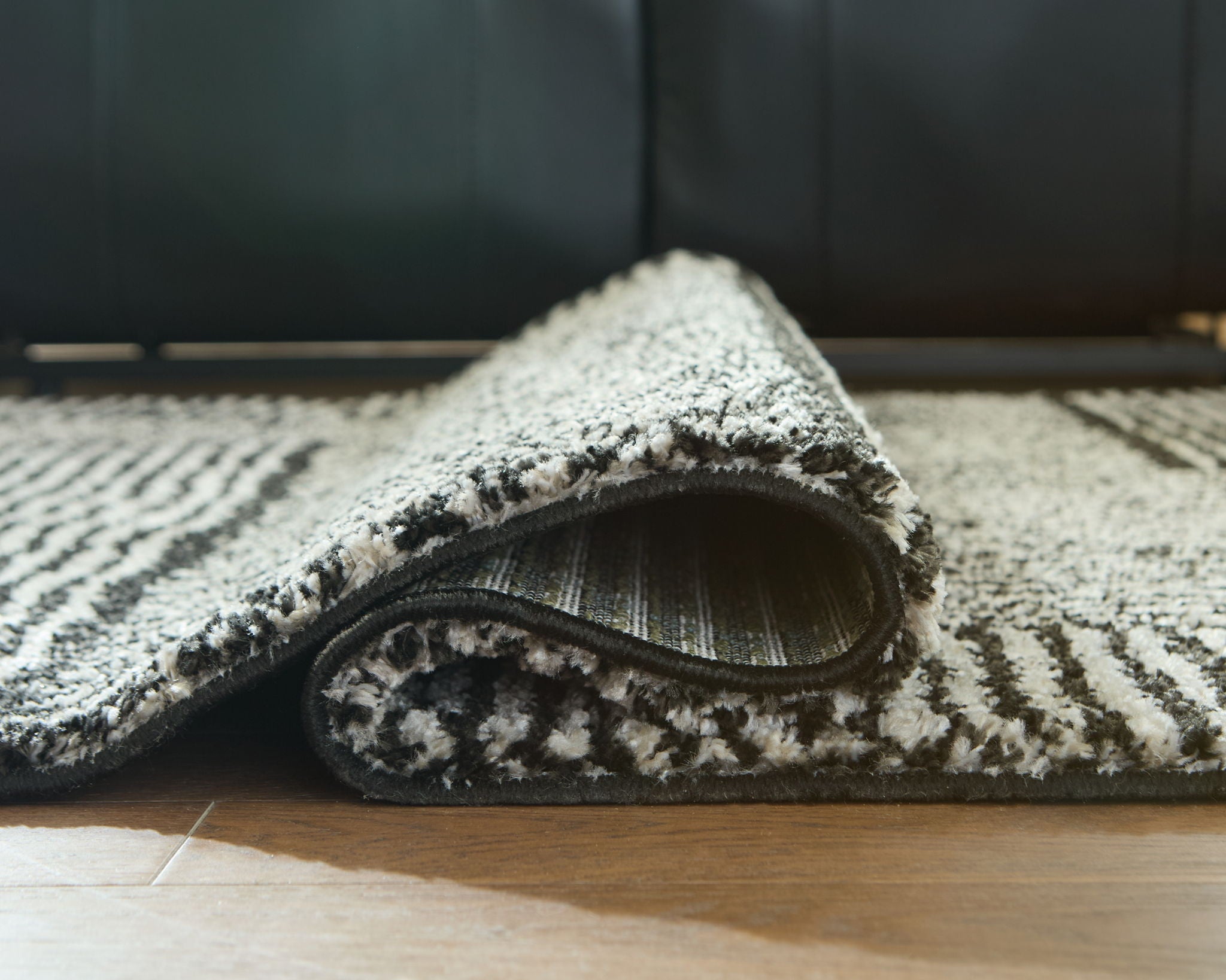 Black-and-white geometric rug with rolled edge, dense textured pile.