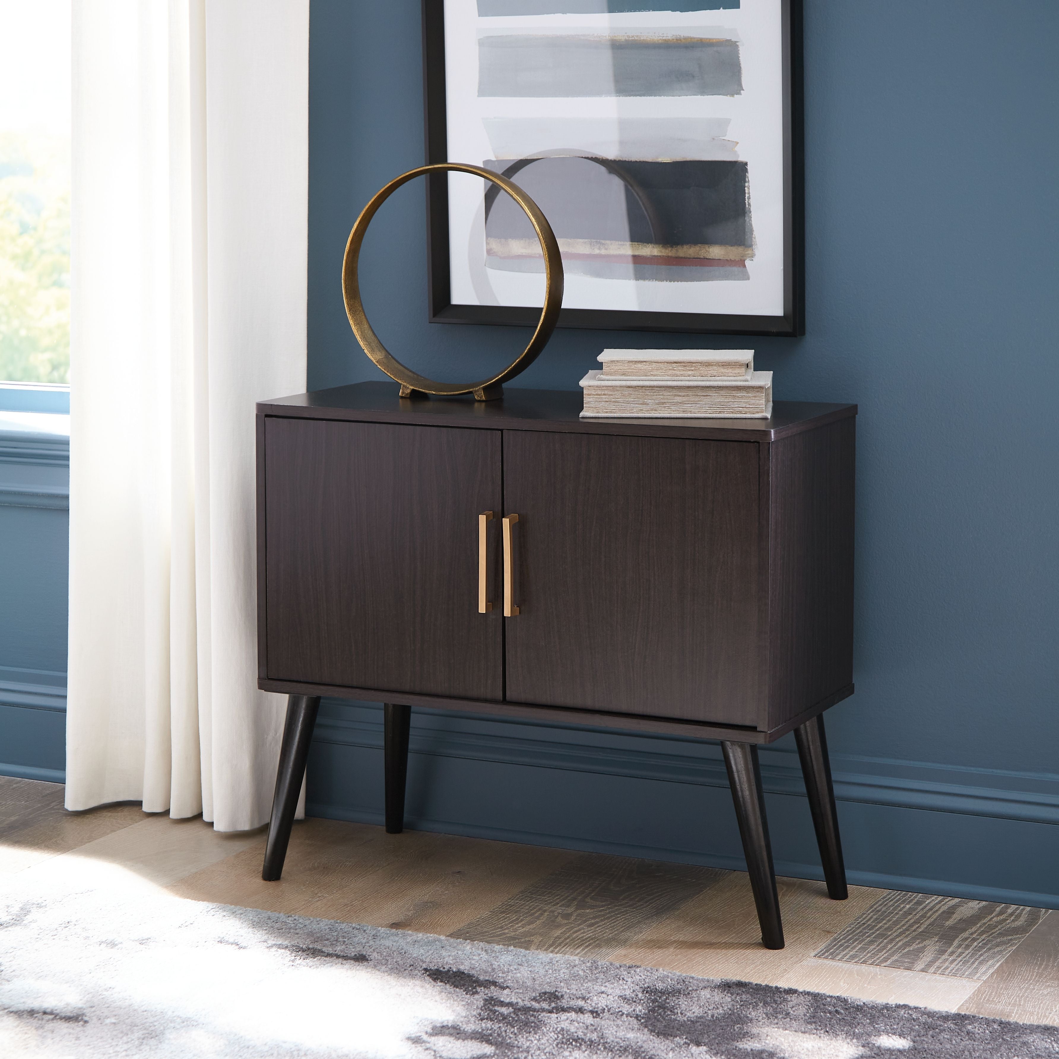 Dark wood accent cabinet with two doors and vertical gold bar handles, standing legs