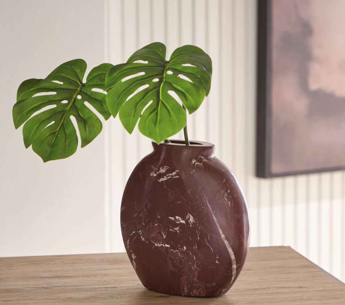 Dark red-brown ceramic vase on table with a green monstera leaf