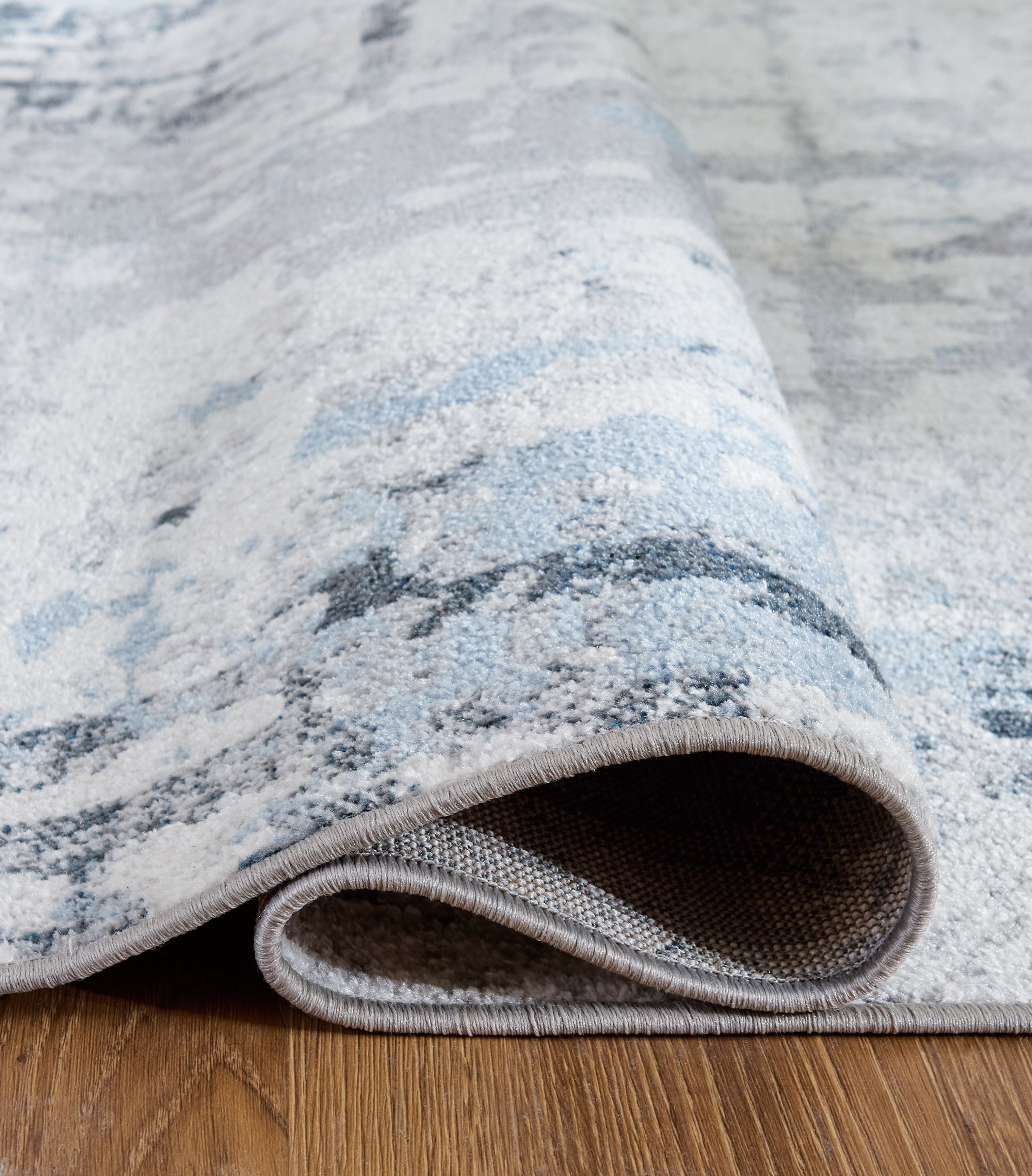 Light blue rug close-up showing textured pile and bound border with gray underside