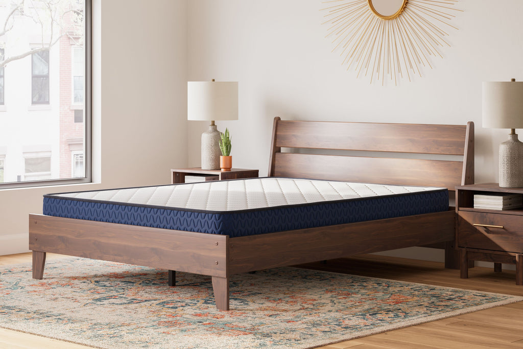 Firm mattress with white quilted surface and blue edge on a light wood bed frame
