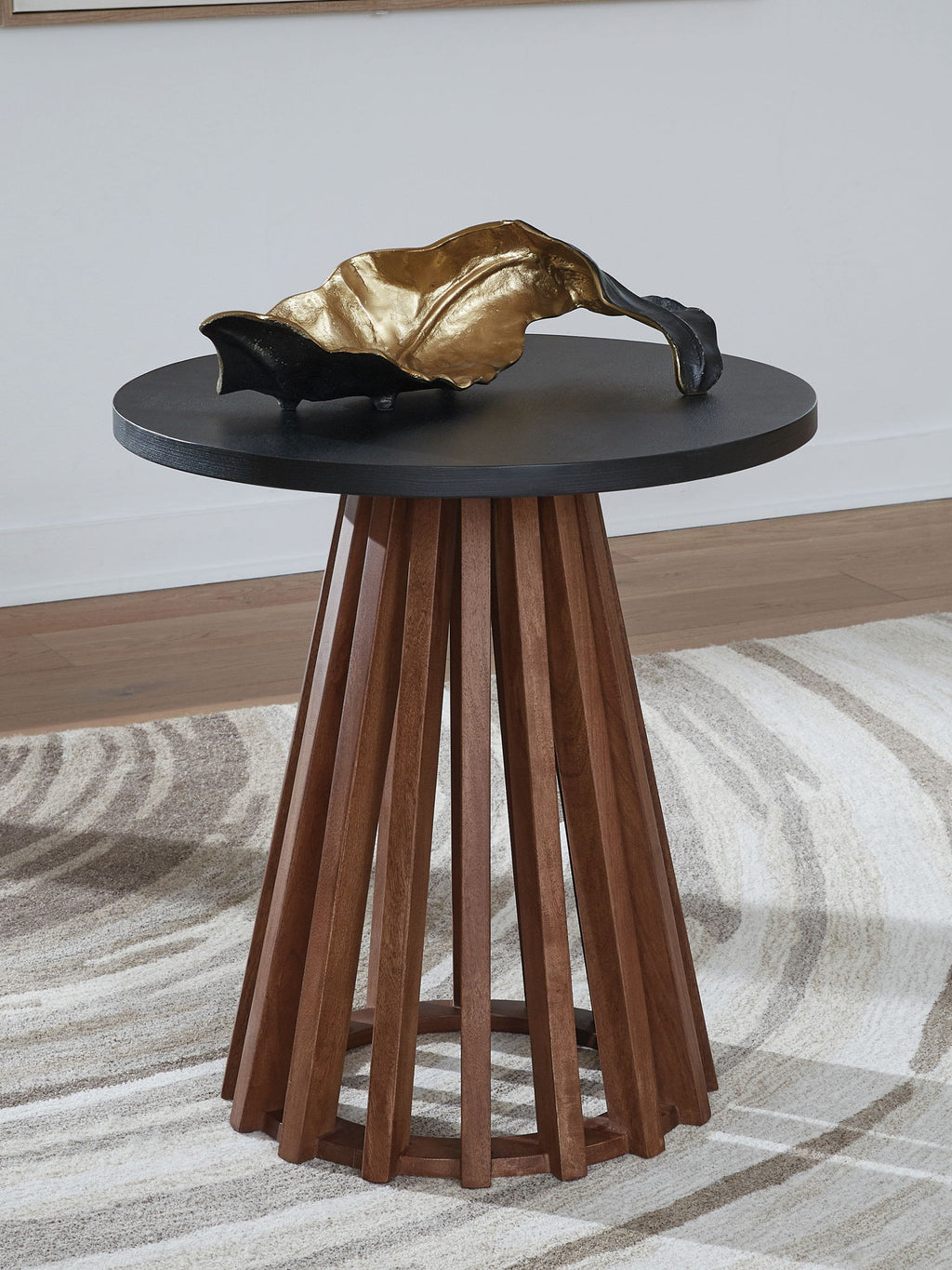 Round end table with dark top and warm brown skirted legs, with gold decor item