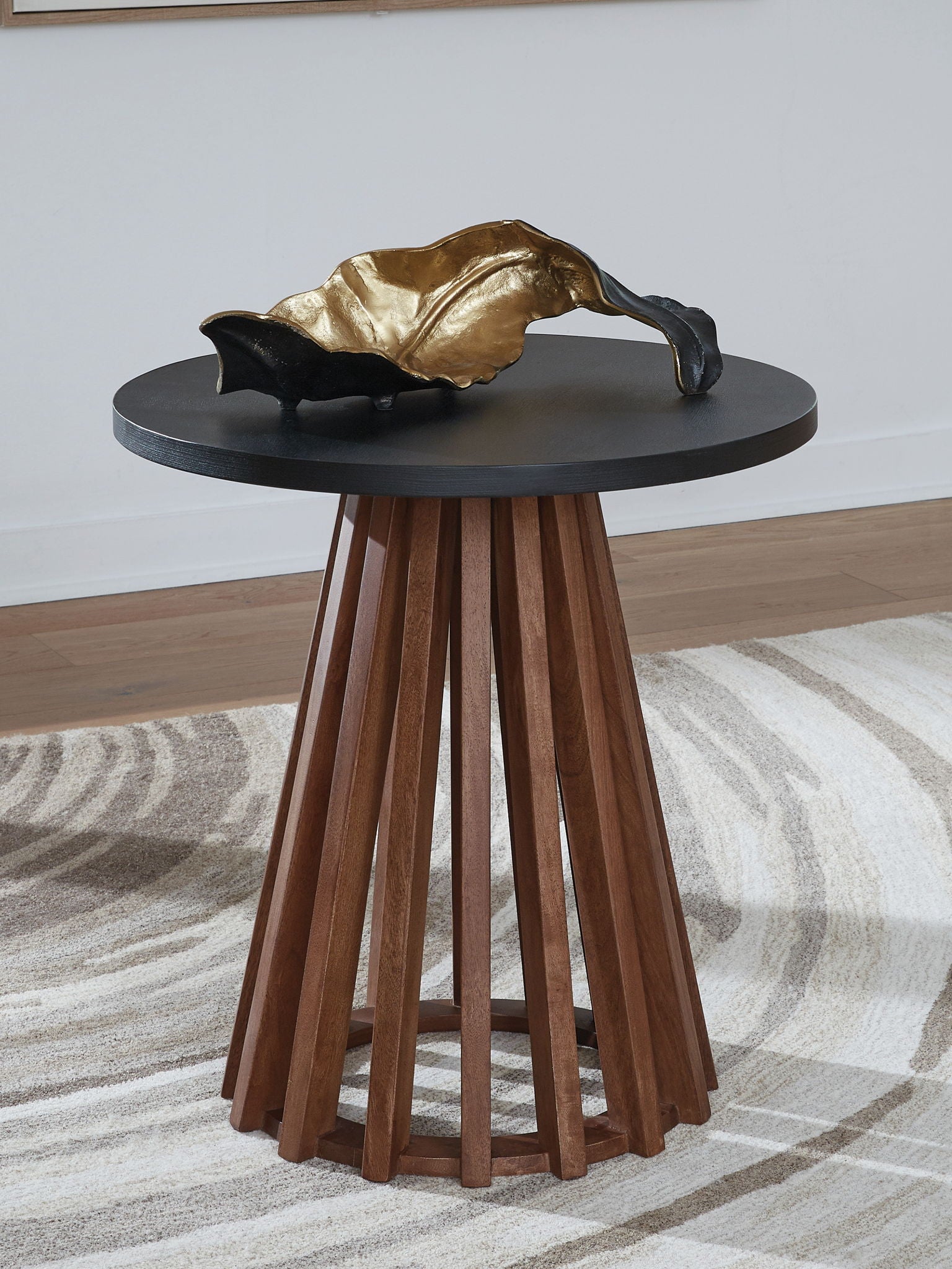 Round end table with dark top and warm brown skirted legs, with gold decor item