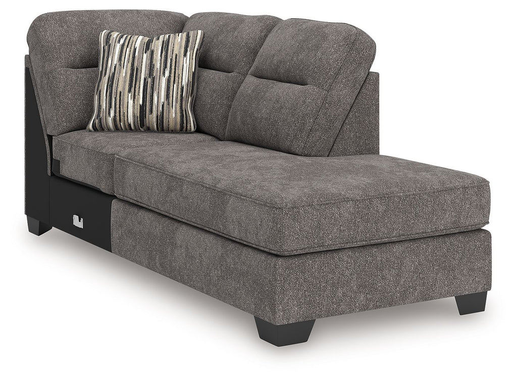 Corner chaise in dark gray fabric with rounded arm, tufted back, black legs; striped throw pillow.