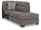 Corner chaise in dark gray fabric with rounded arm, tufted back, black legs; striped throw pillow.