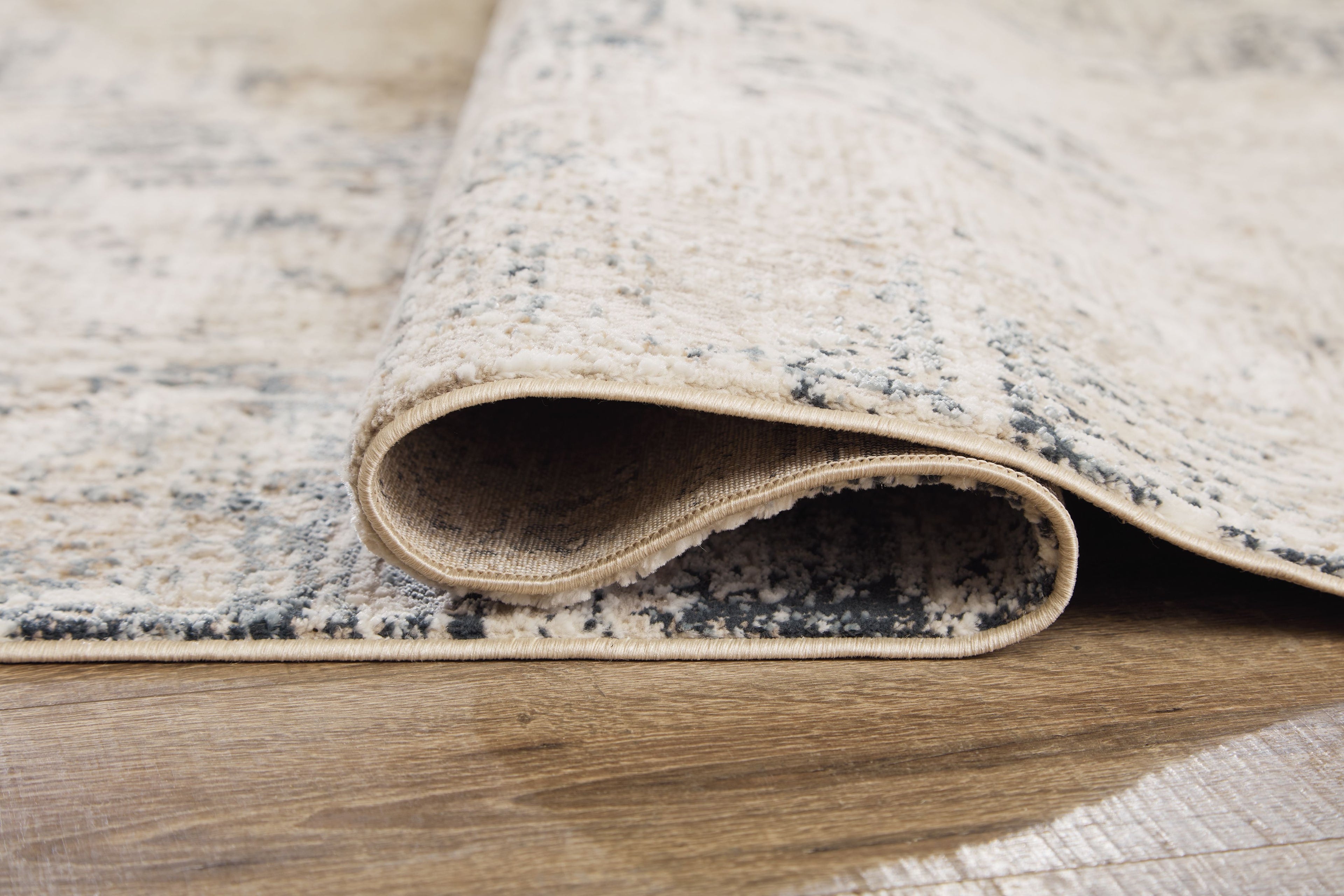 Cream abstract area rug with blue-gray distressed pattern; underside and binding visible.